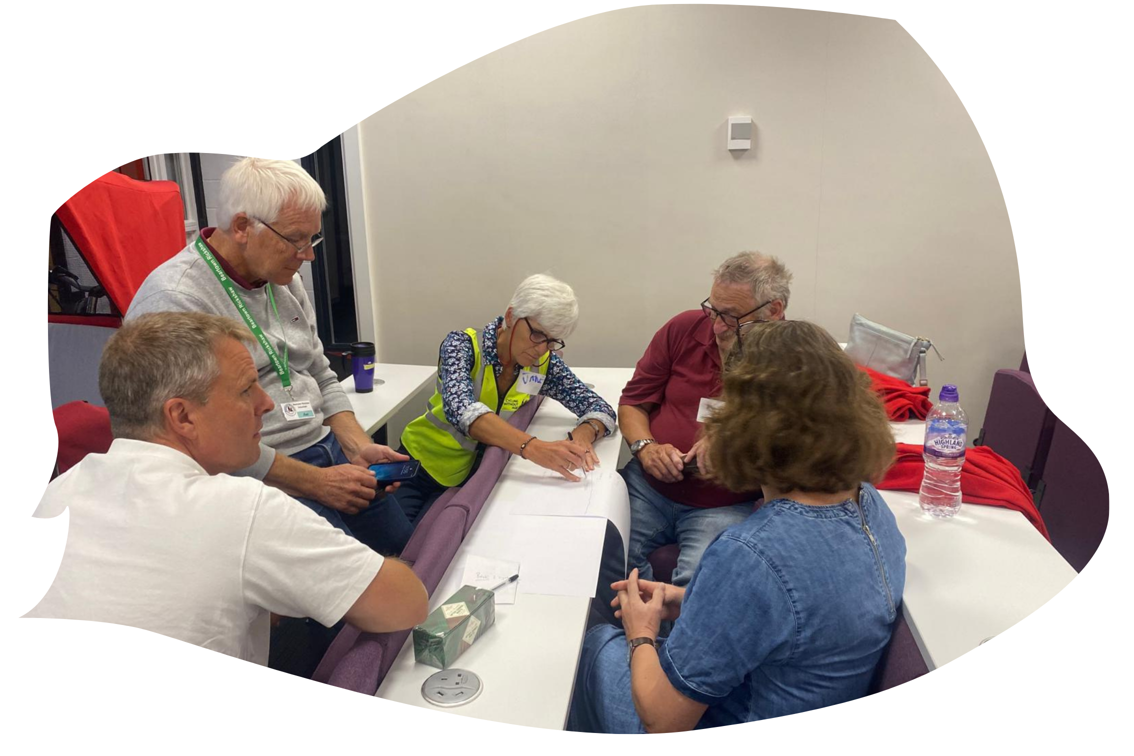 A group of volunteers are at a conference. They are taking part in an interactive activity, writing on a piece of paper. There are 5 of them huddled together.