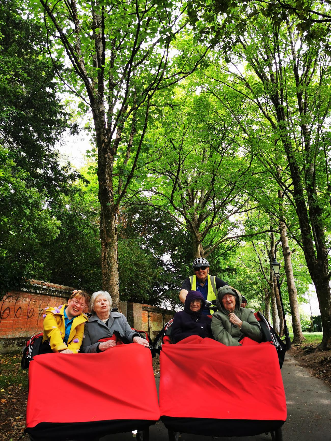 Two red trishaws with big blankets covering the the passengers, are surrounded by green trees in a forest