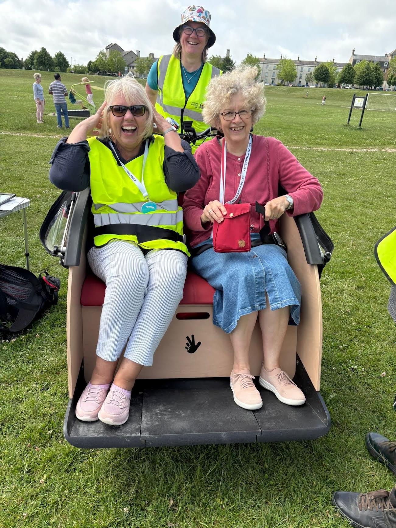 A passenger and volunteer sit in a trishaw in a green field