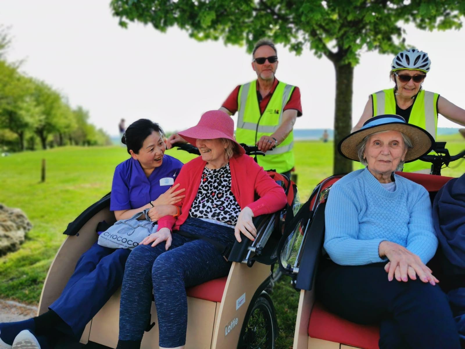 A close up of 2 trishaws with two ladies on one of the bikes, one on the other. They are laughing and chatting. There are too volunteers wearing high visibility jackets.