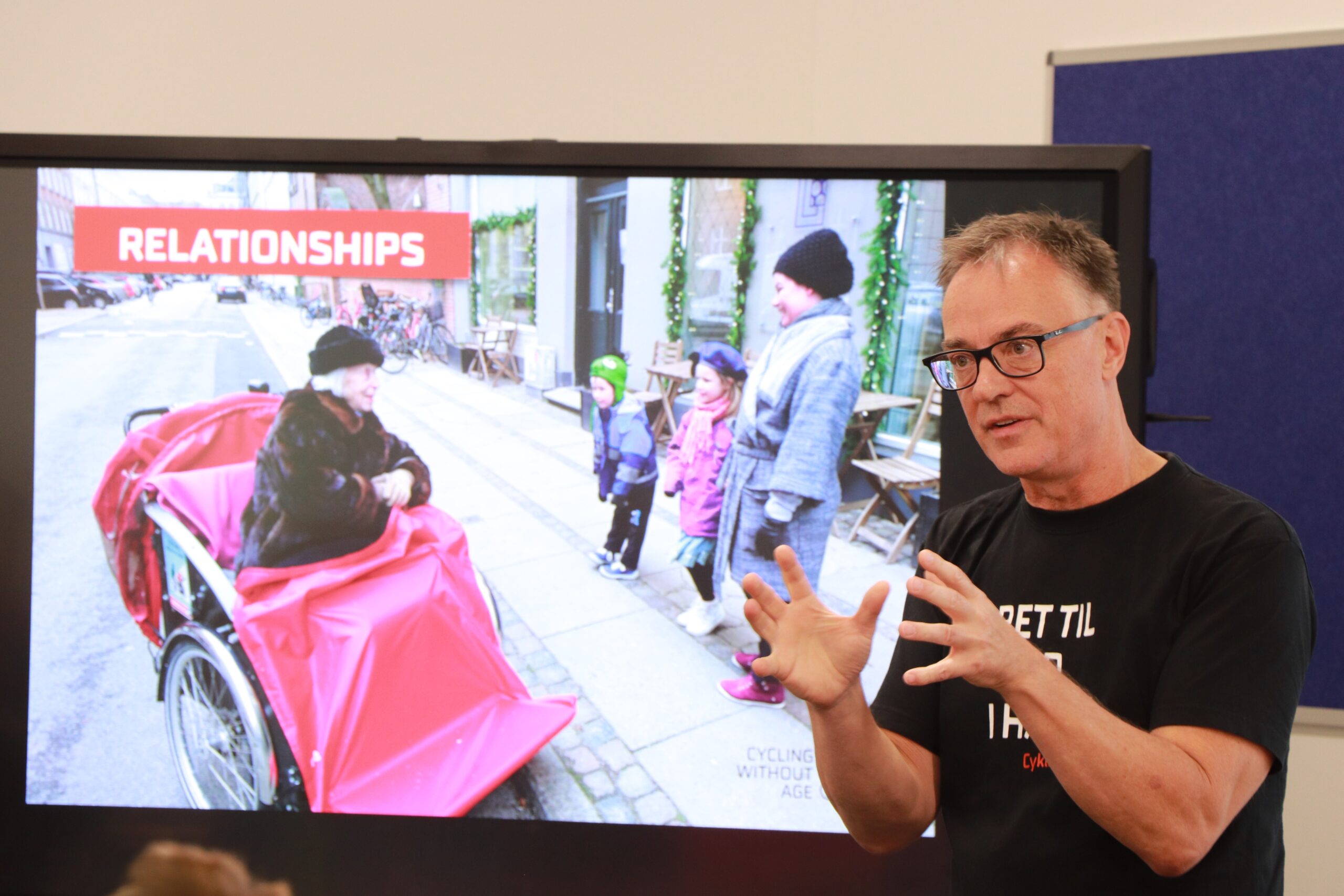 CWA founder Ole Kassow, gives a presention, in the background is a TV screen with trishaws. Ole is animated and focused as he talks.