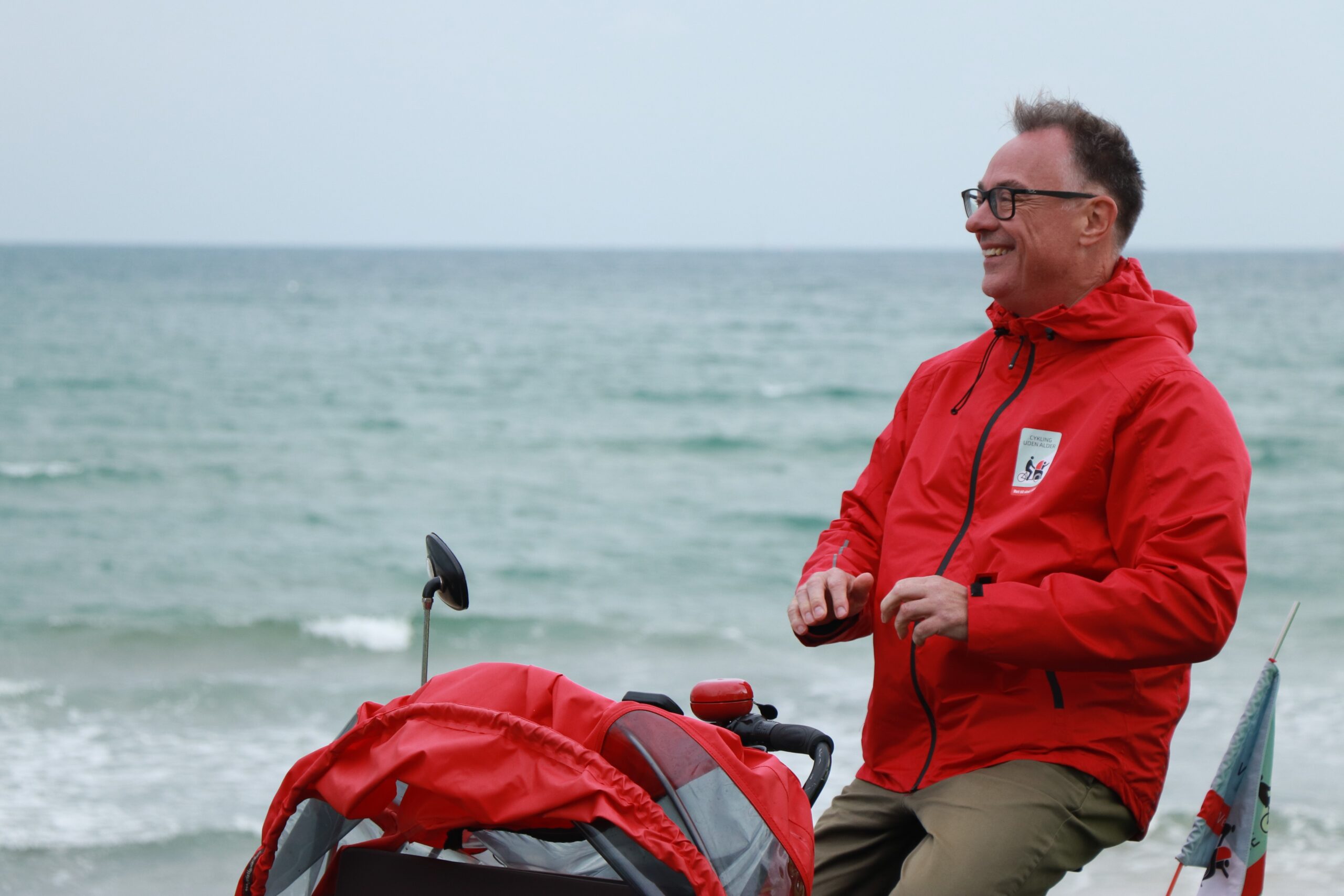 Our founder Ole Kassow rides as a volunteer on one of the bikes, you can see the Weymouth seafront behind him.