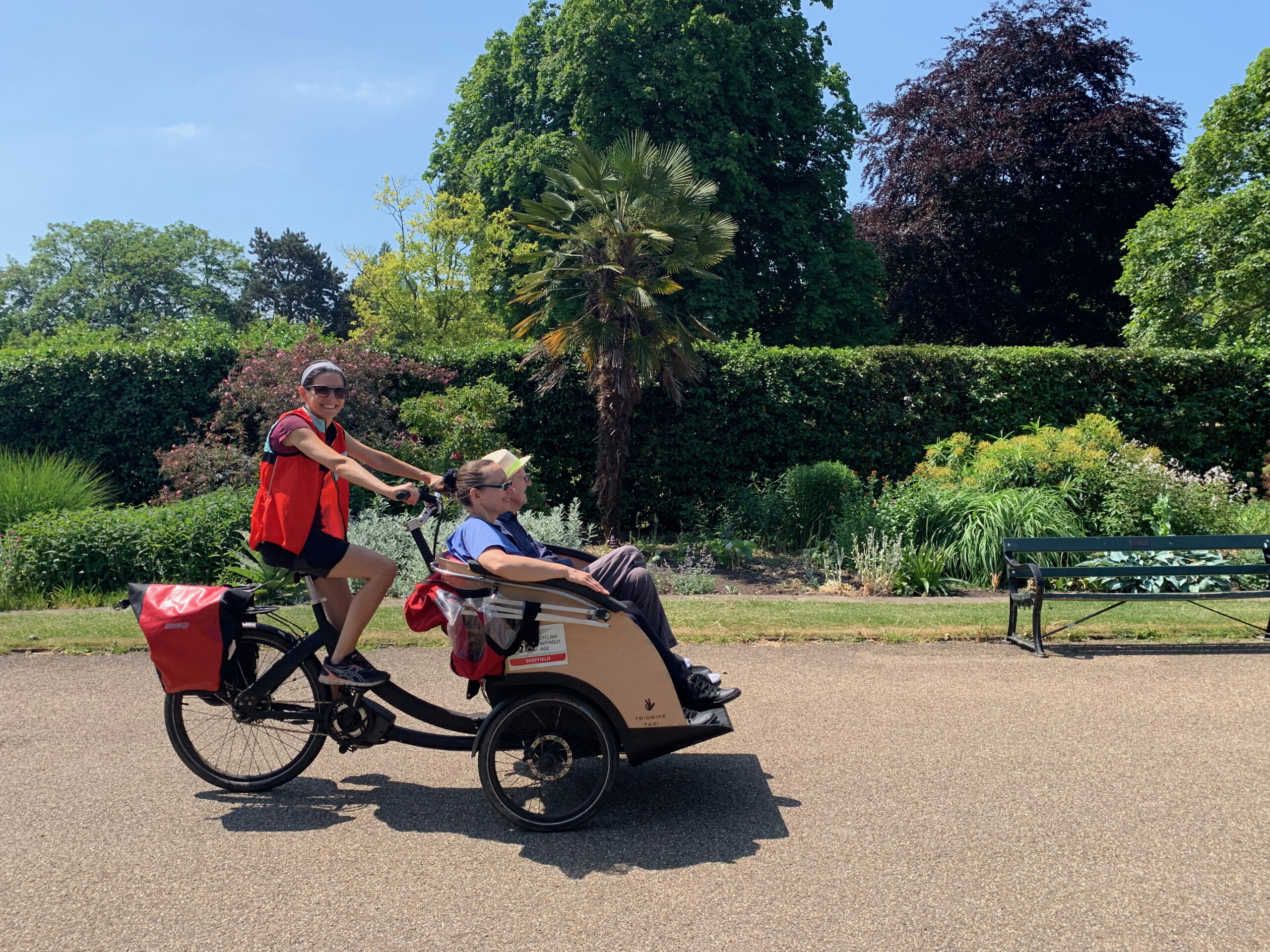 In a botanical gardens a volunteer gives a passenger a ride on a trishaw.