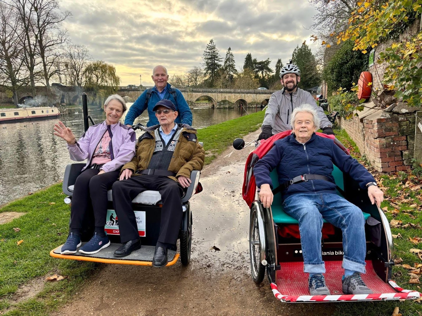 Two volunteer are giving trike rides to three passengers by the river Thames.